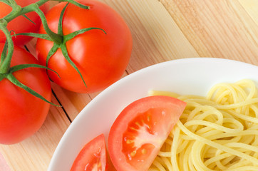 plate of tasty pasta with cut tomato and whole tomatoes at background.