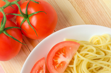 plate of tasty pasta with cut tomato and whole tomatoes at background.