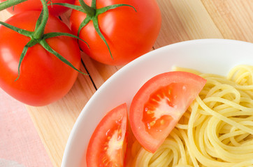 plate of tasty pasta with cut tomato and whole tomatoes at background.