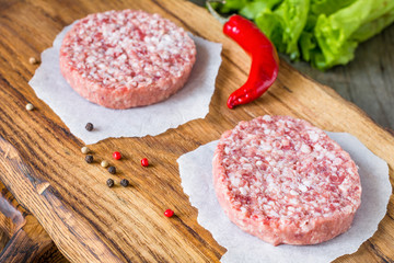 Raw fresh burger meat patties on wooden chopping board