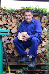 Mann mit gehacktem Holz sitzt auf Holzstoß