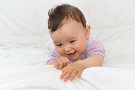 Cute baby girl lying on her stomach in bed and playing