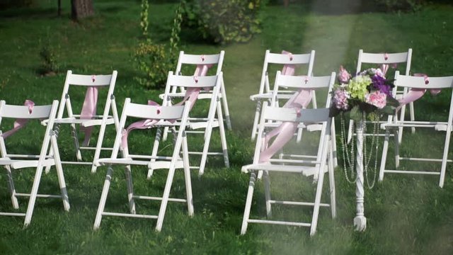 White chairs with pink bows waving in the wind. Wedding decor for registration in the open air.