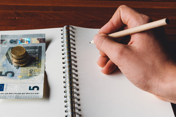 Hand with pencil on blank notebook with euro money