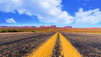 Fototapeta na wymiar Panoramic view on monument valley in Arizona and Utah from the middle of the road at forrest gump point with typical yellow us highway road marking and a beautiful blue cloudy sky