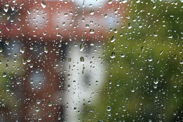 Rain drops on window with building and green tree in background 