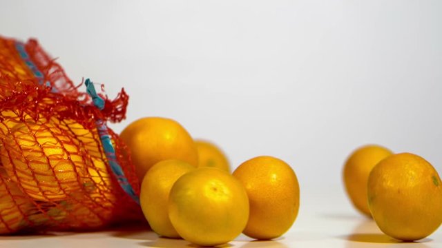 Slow motion of falling sack and orange tangerines that are getting out of it. On white background