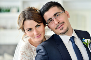 Wedding couple indoors is hugging each other. Beautiful model girl in white dress. Man in suit. Beauty bride with groom. Female and male portrait. Woman with lace veil. Cute lady and handsome guy