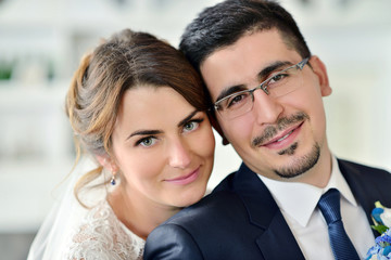 Wedding couple indoors is hugging each other. Beautiful model girl in white dress. Man in suit. Beauty bride with groom. Female and male portrait. Woman with lace veil. Cute lady and handsome guy