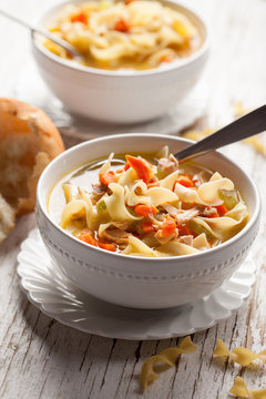 Homemade Turkey Noodle Soup with piping hot rolls on weathered white wood