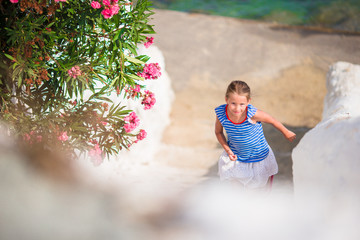 Adorable girl having fun outdoors. Kid at street of typical greek traditional village with white walls and colorful doors on Mykonos Island, in Greece