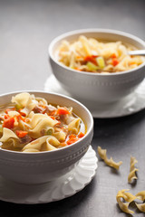 Homemade Turkey Noodle Soup with piping hot rolls on grey background