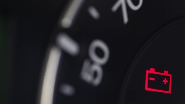 Close up footage of a car's dashboard, with the battery warning light coming on.