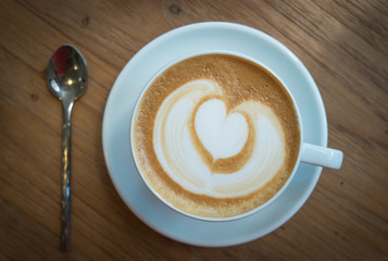 A Cup of hot latte art coffee on wooden table. A cup of hot latte art coffee with heart pattern. hot milk art coffee on wooden table. Vintage latte art coffee.