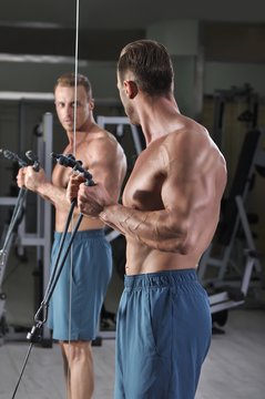 Handsome powerful athletic man doing biceps exercise with cables. Strong bodybuilder with perfect muscles.