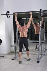 Fototapeta premium Handsome powerful athletic man doing barbell shoulder press exercise. Strong bodybuilder with perfect muscles.