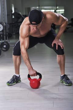 Handsome powerful athletic man performing kettle bell exercise. Strong bodybuilder with perfect shoulders, biceps and triceps.