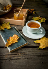 Cozy autumnal mood, warm autumn. A cup of hot tea with lemon and ginger on a rustic table, plaid, yellow leaves, honey and a book to read. Top view