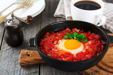Shakshuka with tomato sauce and fried egg in a cast iron pan for breakfast on the old wooden background. Rustic Style, Selective Focus.