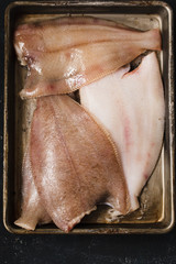 Raw platessa fish in a baking alluminium tray, seasoned with salt and olive oil. Top view