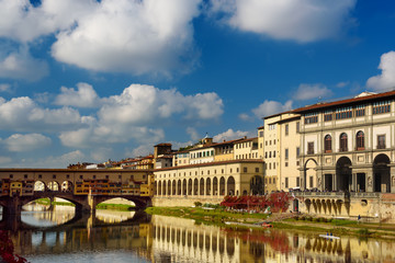 Fototapeta na wymiar View from the river to the famous italian medieval bridge - Ponte Vecchio in Florence with blue sky and clouds, travel outdoor Italy sightseeing background