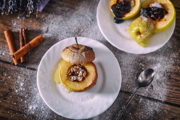 stuffed baked apple with nuts, honey and chocolate on white dessert plates, dark wooden background. Christmas sweet. healthy eating concept.