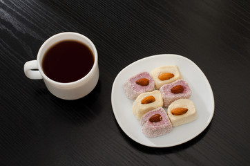 Coffee mug, saucer with Turkish Delight on a black table, top view