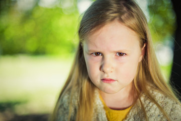 Fototapeta premium Angry at her parents a little girl sitting on a park bench.