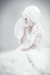 Vintage inspired modern photograph of beautiful woman in a white gown holding a hand fan.