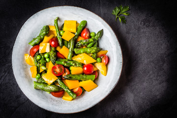 Vegetarian salad with asparagus, cherry tomatoes, bell pepper, slate background
