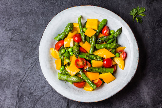 Vegetarian salad with asparagus, cherry tomatoes, bell pepper, slate background