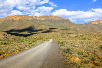 African safari in 4x4. Adventure in the African desert. Gravel mountain road in the dramatic sky, Karoo National Park in the summer, Western Cape province of South Africa.