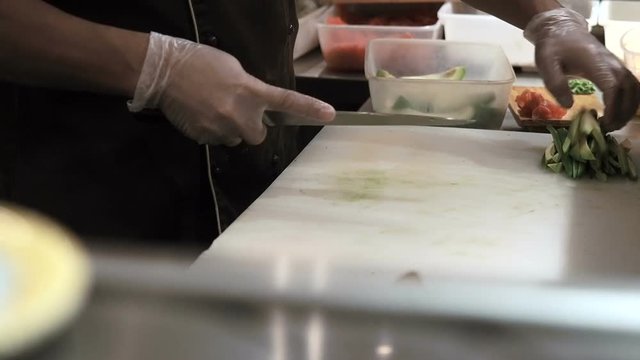 Process of making sushi rolls. Man cutting up green rite avocado by slices. Prepared sushi rolls pass through on foreground