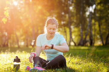 Woman runner sitting on the grass using a smart watch.