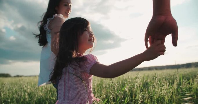 little Asian girl walking on the green field with their parents, holding hands, slow motion