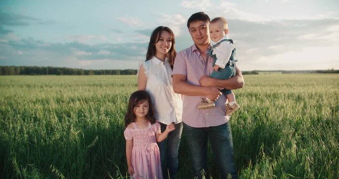 portrait of young happy Asian family standing in a green field with two children looking at the camera and smiling, slow motion