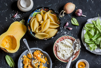 Raw ingredients for making pumpkin and ricotta stuffed shells. Pasta shells, pumpkin, spinach, ricotta. On a dark background, top view. Flat lay