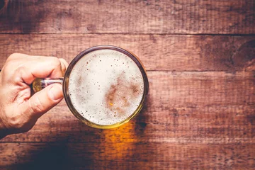 Fotobehang Bier Hand holding a glass of beer on wooden table