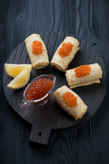 Black wooden serving board with rolled crepes and red caviar