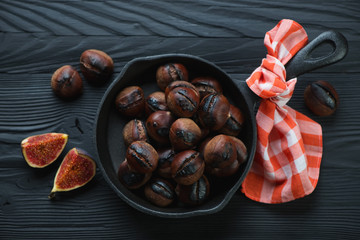 Frying pan full of roasted chestnuts on a black wooden surface