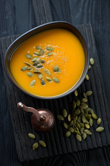 Bowl with pumpkin cream-soup over black wooden surface, top view