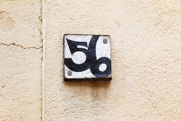 House number plate fifty six 56 on old plastered wall, wooden placard.
