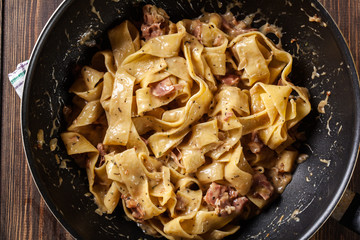 Pappardelle pasta with prosciutto and cheese sauce on pan