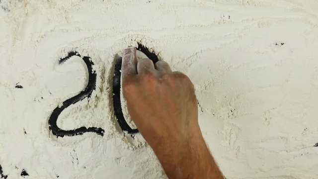 Young man writes a word numbers 2017 on white flour