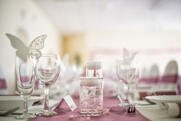 Close-up detail of wedding table decoration in pink and white color pallete made of candles in glass and paper ornaments in shape of butterflies.
