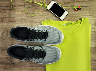 Set for sports: shoes, t-shirt, mobile phone with headphones  close-up on a wooden background, top...