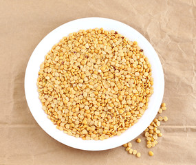 Toor dal, also known as split pigeon pea, rich in proteins, in a plate on a crumpled brown paper background.