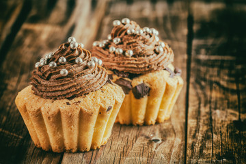 Vanilla cupcake with chocolate topping. Old wooden background.
