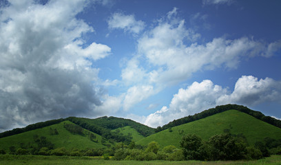 Lush green hiils againsblue sky with wite clouds