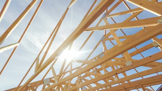 Roof beams of a modern American home in mid construction phase, looking up toward blue sky with sunlight